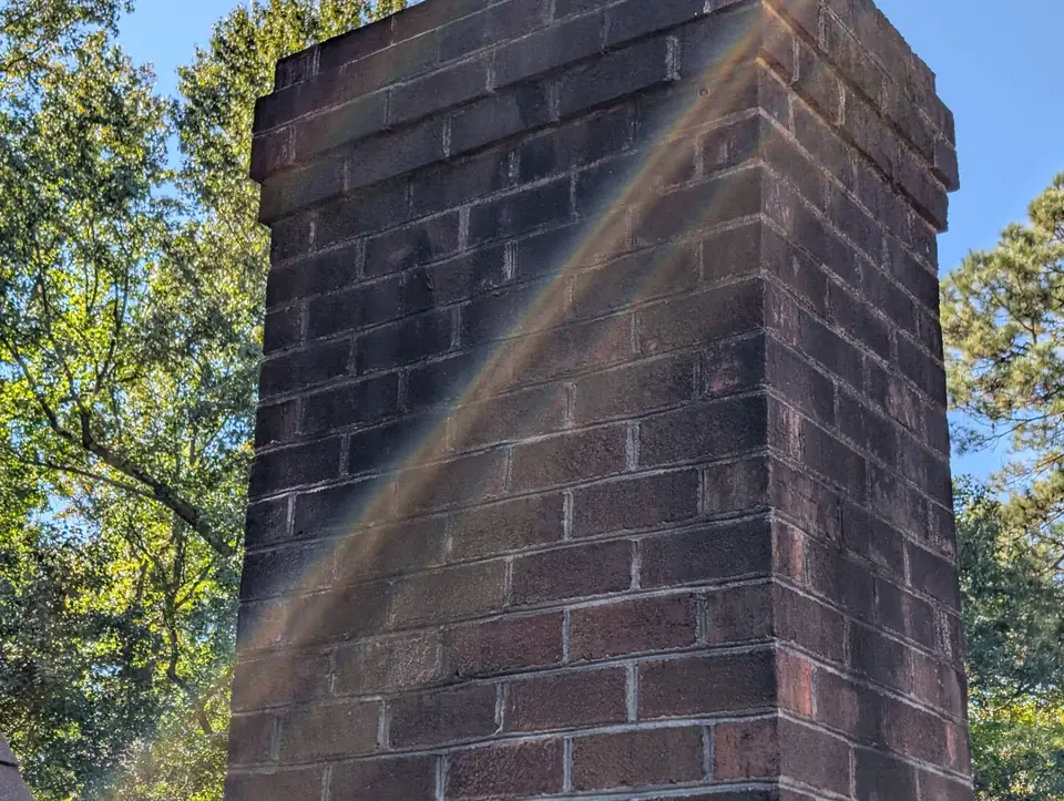 Brick chimney stack rising above the roofline against trees