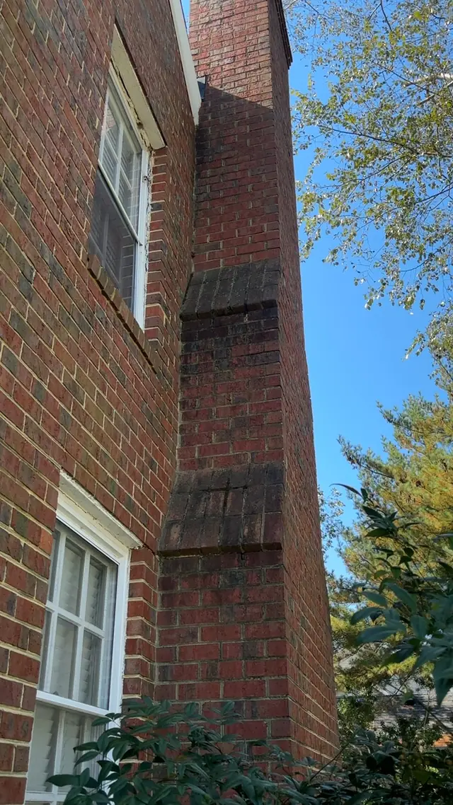 Tall exterior brick chimney beside a two-story home