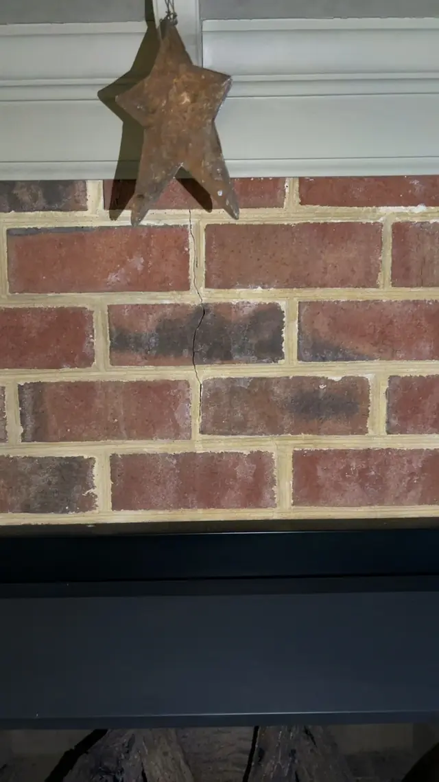 Hairline crack running through brick above a fireplace opening